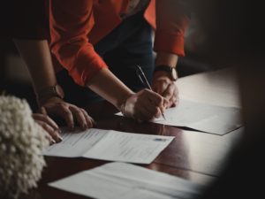 An image of two people bending over and inspecting and signing documents.